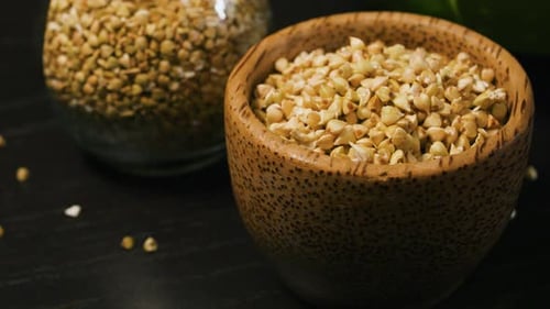 Sprouted Raw Green Buckwheat in Wooden Cup and in Glass Jar Black Background