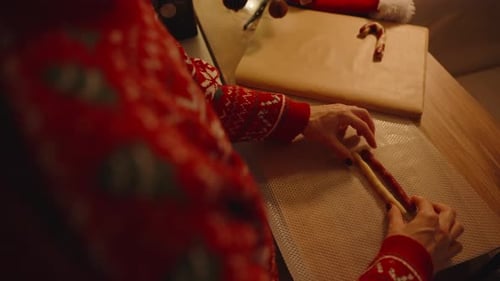 Woman Twisting Red and White Dough into Candy Cane Shape over Textured Mat Viewed from Overhead