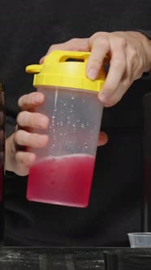 Vertical video. A Variety Of Vitamins And Supplements For Sports On The Table, A Man Drinks A Red