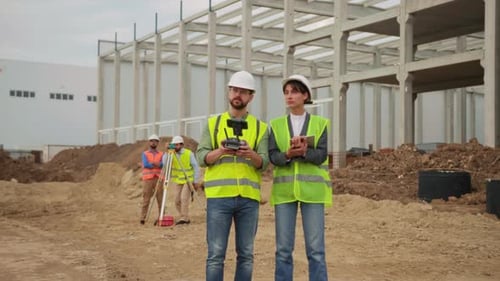 Shooting of Team of Construction Workers Wearing Brightly Yellow Vests Controlling Drone Man and