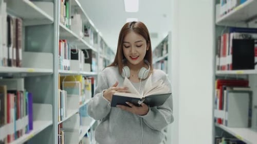 Asian young student girl in sweater reading the book from bookshelf in university or college library