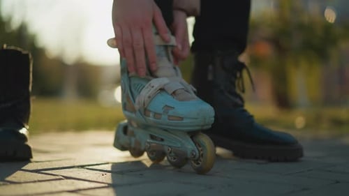 Person Fastening Rollerblade Straps While Wearing a Black Boot in a Park