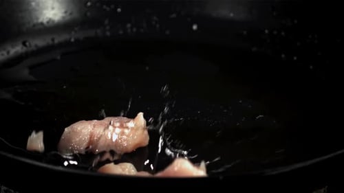 Chicken Pieces Splashing into a Pan with Oil