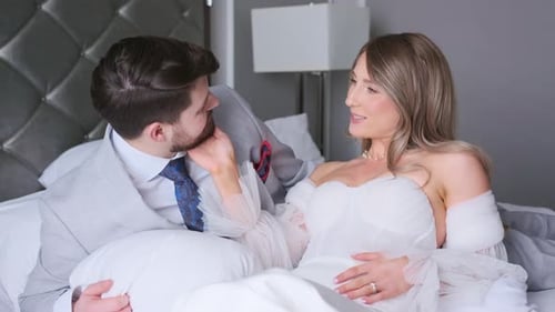 Loving couple in elegant loungewear relaxes on bed. Romantic, honeymoon, wedding.