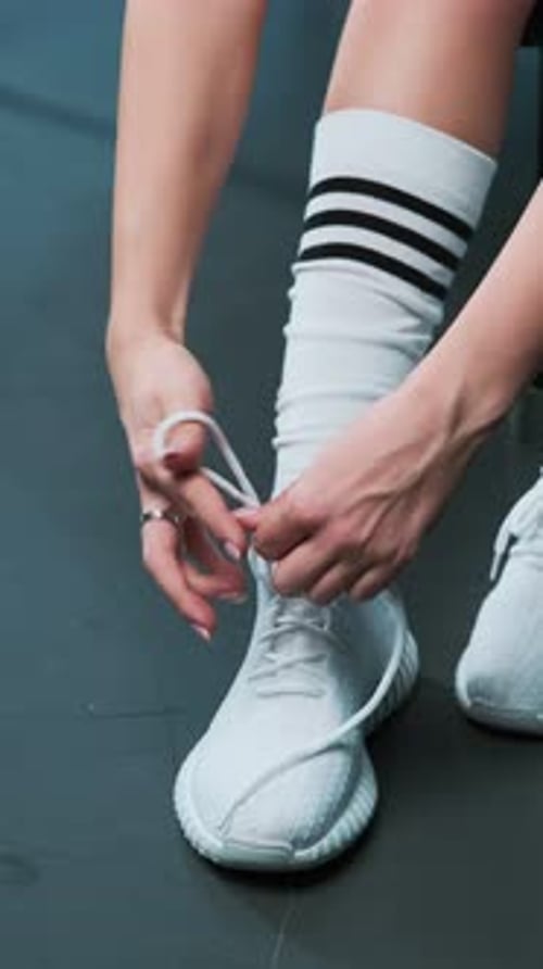 Close-up of legs of energetic young fitness girl in white sneakers tying laces. Jumping workout. Hig