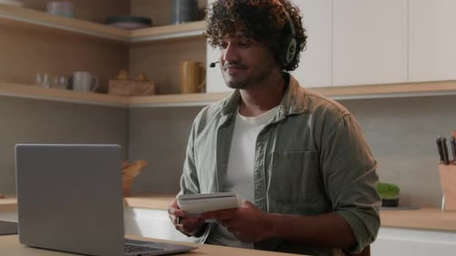 Young Adult Taking Notes During Video Call in Kitchen