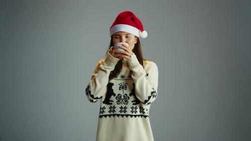 Cute Woman Drink Hot Cup of Tea Christmas Sweater Santa Hat Studio Background