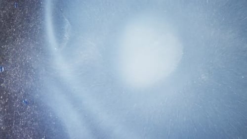 shot of white alcohol ink diffusing in vibrant blue liquid with dreamy textures