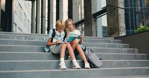 Cheerful high school students sitting on stairs street outdoors near campus talking smiling