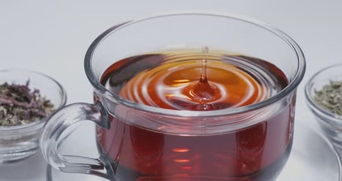 Drop slowly falls into a glass cup of tea.