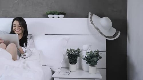 Woman using tablet in bed, puts on glasses