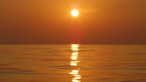 Bright glowing summer sun setting above rippling golden color ocean