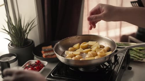 Potatoes sizzling in pan, cook adds salt and pepper