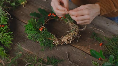 Person Crafting a Holiday Wreath at Table