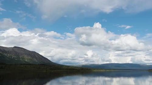Zeitraffer eines ruhigen Sees mit Bergen im Hintergrund und Wolken, die sich in der Ferne schnell bewegen