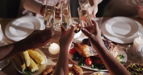 A Group of People Clink Glasses of Champagne Over a Festive Table Where Roasted Turkey is Served Top