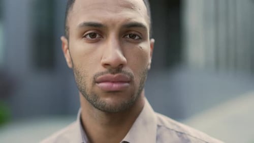 Close up of a portrait of a young adult man in a shirt who looks seriously on the camera