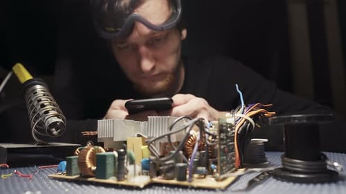 Man Soldering Electronic Components on Workbench