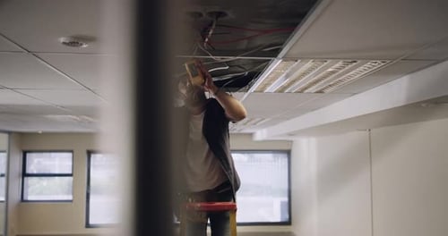 Man Inspecting Wiring on Ladder at Workplace