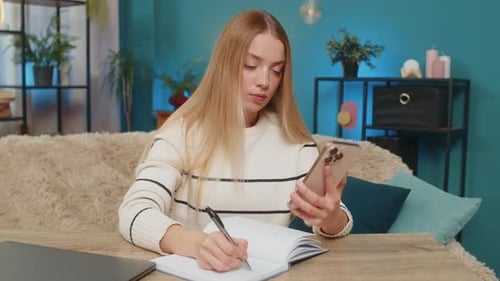 Woman Using Phone and Writing at Home