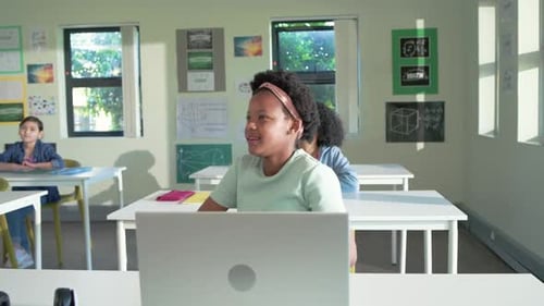 African American classmates watching preteen girl at front desk laptop smiling at passing teacher