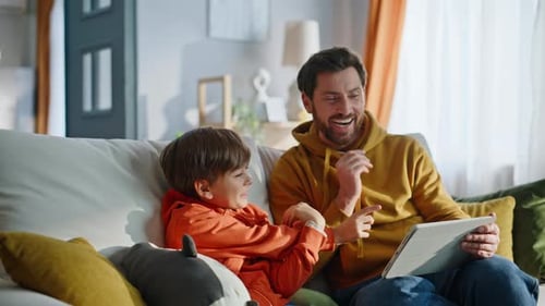 Dad and Son Interact with Tablet on Sofa