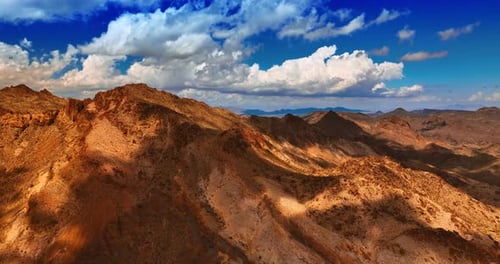 Brown rocks contrasting with azure skies. White cloudscape hanging over the mountains in Mojave