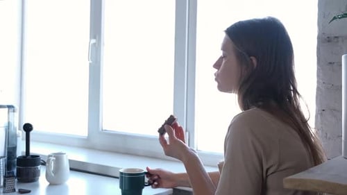 woman eating bar of chocolate with coffee in the kitchen table
