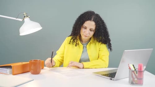 Woman Reviews Document at Desk with Laptop