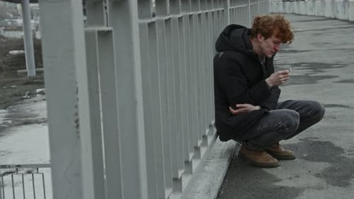 Jeune homme souffrant de douleur émotionnelle qui fume alors qu'il est accroupi près de la balustrade