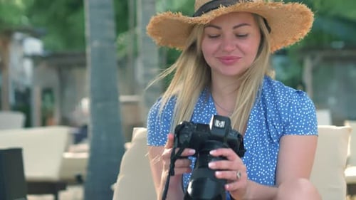 Photography and Travel A Young Woman in a Hat Holds a Camera and Takes Pictures on the Beach
