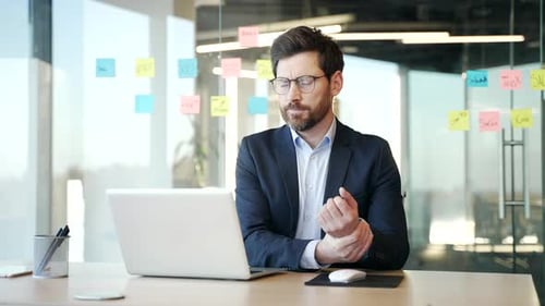 Professional Man Massaging Wrist at Desk in Office
