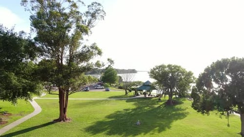 Fliegen Sie über einen Park am See mit Pavillon, während Spaziergänger auf einer wunderschönen Quelle durch das Gras wandern