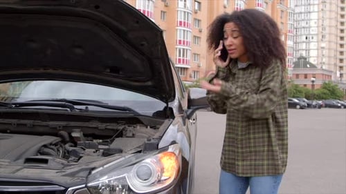 Upset Woman Talking on Phone Next to Broken Car
