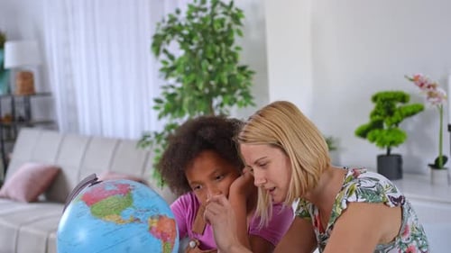 Girl and Woman Examining Globe Indoors