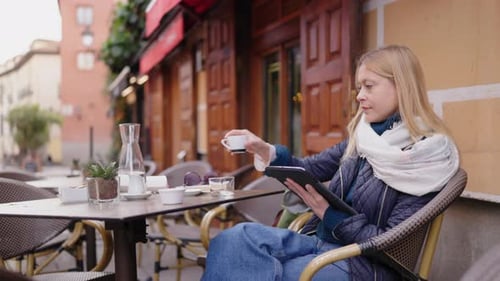 A Young Woman is Enjoying a Delicious Cup of Coffee While Using Her Tablet at an Outdoor Cafe