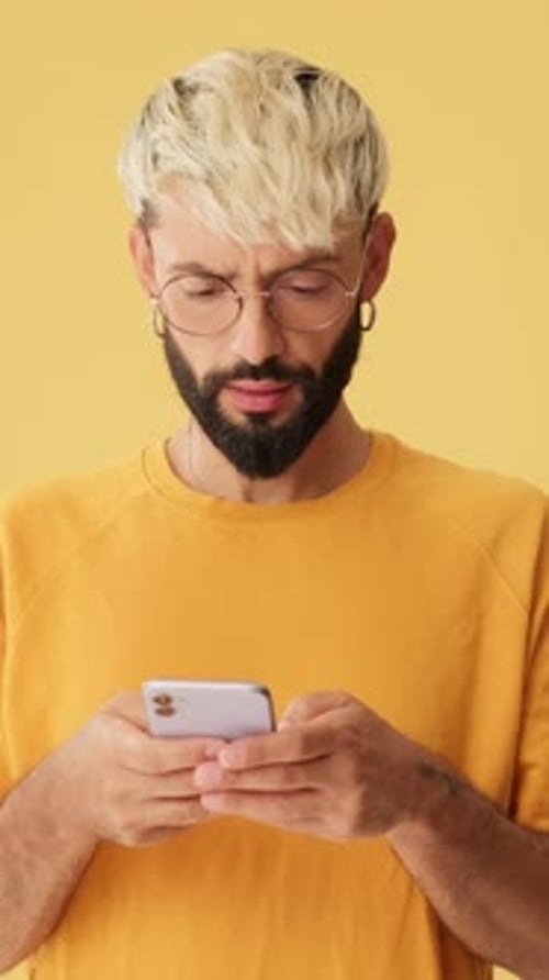 Man with phone in his hands is surprised, wow, isolated on yellow background in studio