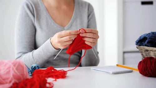 Woman knitting a red scarf at home