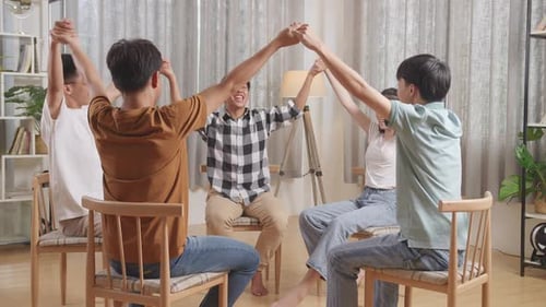 Asian Teen Group Sitting In Chairs Forming A Circle Discussing At Home. Take Each Others Hands