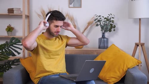 Young Man Puts on Headphones and Uses Laptop