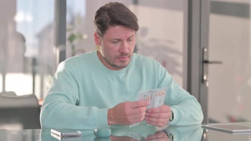 Man Counts Money Indoors at Desk