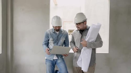 Asian bearded Indian engineer wearing helmet Check blueprint and decoration designs from laptops for