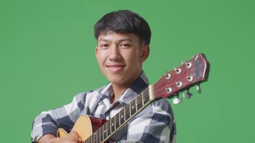 Close Up Of Asian Teenager With Guitar Crossing His Arms And Smiling On Green Screen Background