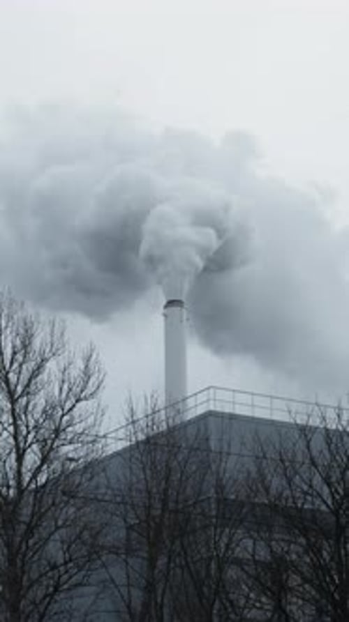 Plumes of Smoke Rising From Chimney Atop Building Tainting the Sky