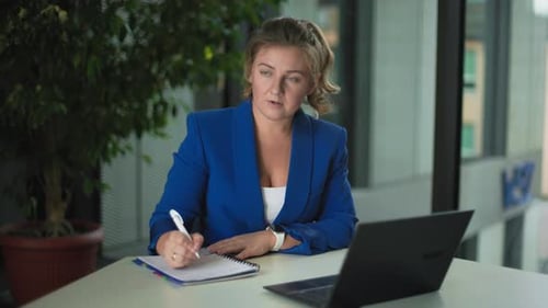 Conférence en ligne Une jeune femme d'affaires prend des notes dans un bloc-notes et discute avec ses collègues en ligne via