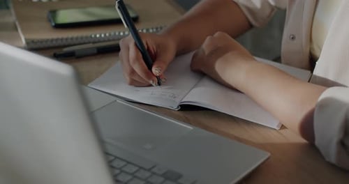 Young Adult Writing Notes Next to Laptop