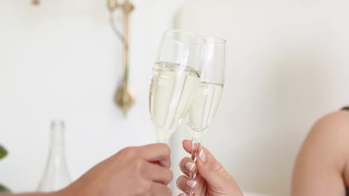 Deux mains font tinter des flûtes, la gauche s'éloignant tandis que la droite tient, célébrant dans une pièce pâle