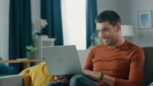 Smiling Young Man Using Laptop on Couch