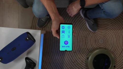 Top View Close Up Shot of Man on the Couch Holding Smartphone Using App to Turn on Light Speaker and