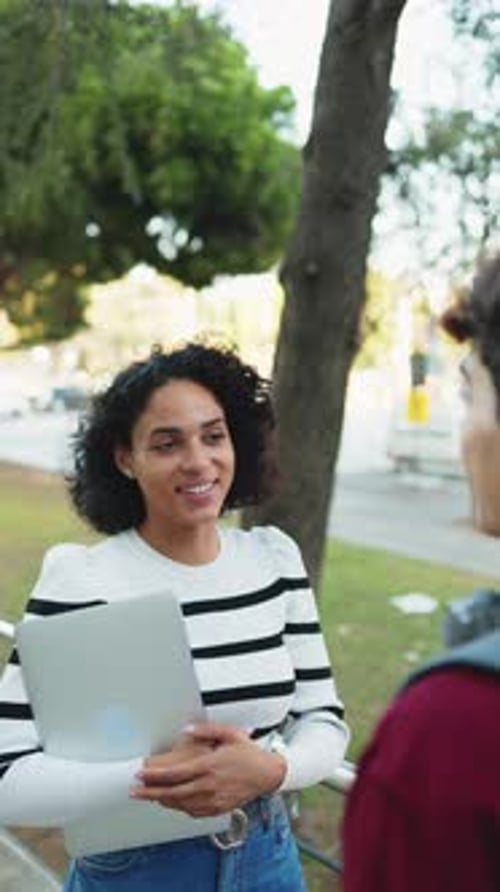 Young latin student girl talking to her college classmate on campus in the sunlight